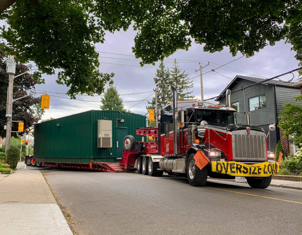Scott-Woods Transport truck hauling oversized green container through residential street