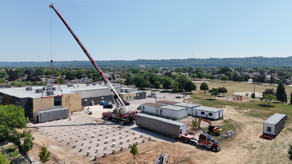 Specialized transportation and crane support for portable classroom installation at a school project site displaying our modular & portable heavy haul services.