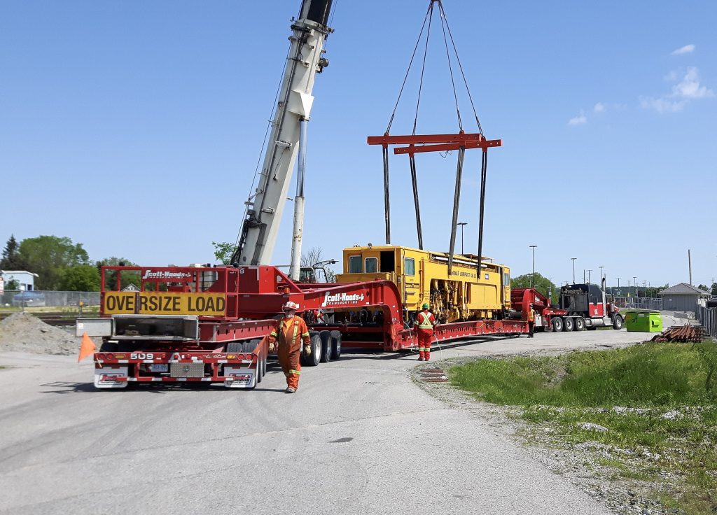 Scott-Woods heavy haul fleet transporting oversized rail maintenance equipment with crane and specialized trailer support.
