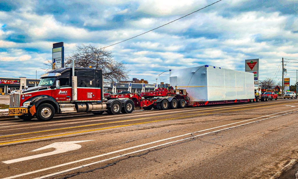 Scott-Woods heavy haul fleet transporting an oversized modular unit through an urban transportation route.