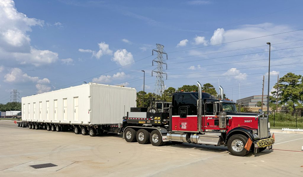 Scott-Woods heavy haul fleet transporting an oversized modular building using specialized multi-axle trailer equipment.